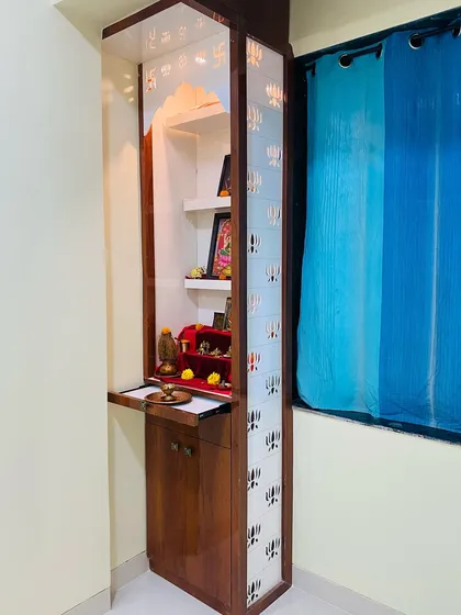 A compact mandir designed for a bedroom, featuring glass doors with a lotus pattern. It includes a pull-out tray for placing diyas and incense.