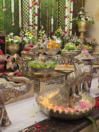 A detailed view of an offering table with silver elephant props, dolls, and bowls of fruit.