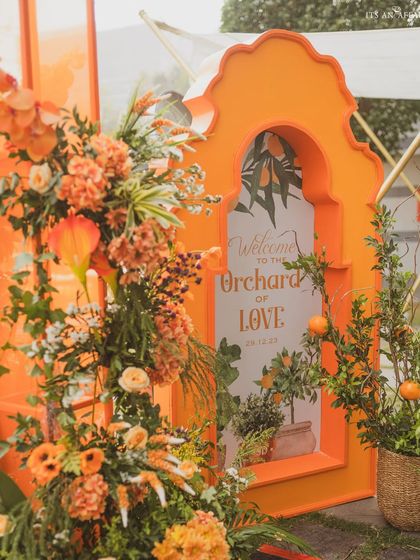 A custom welcome sign for the 'Orchard of Love', framed by an orange arch and surrounded by fresh orange trees.