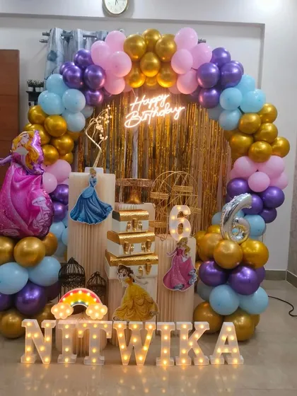 I can create a royal celebration with a Disney Princess theme. This setup for a 6th birthday includes a gold shimmer curtain, a multi-colored balloon arch, princess cutouts, a marquee number '6', and illuminated name letters.
