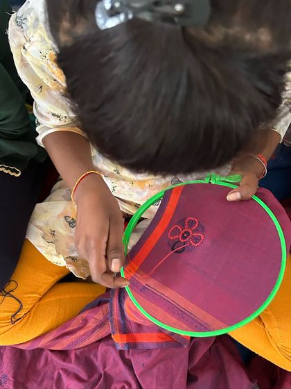 From the handloom to the embroidery hoop, our Chikankari sarees are a testament to the skill of our artisans. This image shows a floral motif being embroidered onto a purple saree.