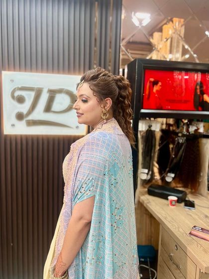 A side view of a fun and flirty party hairstyle, featuring a high curly ponytail and face-framing tendrils.