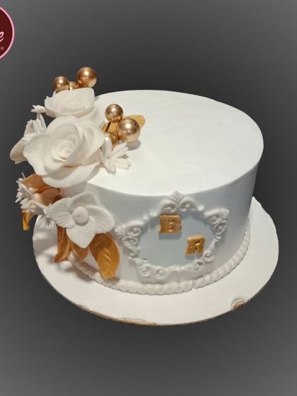 A sophisticated white and gold anniversary cake. This design features delicate white sugar flowers, gold leaves, and a monogram for a personalized touch.