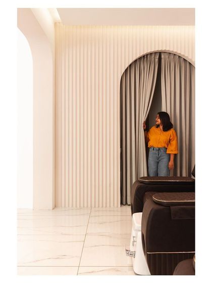A glimpse into a private area of the 'Frumos' salon, framed by a soft archway and curtains. This layering creates a sense of discovery and privacy within the open-plan space.