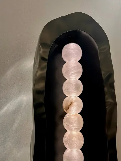 A sculptural floor lamp by Nituṣhā, featuring a stack of illuminated stone spheres within a dark metal shroud. This piece is a powerful example of how light and material can be combined to create a dramatic, artistic statement.