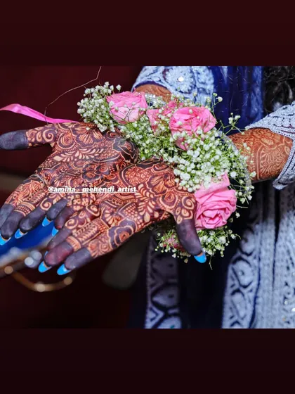 A beautiful shot of the bride's hands adorned with floral bracelets made of pink roses, perfectly complementing the henna stain.