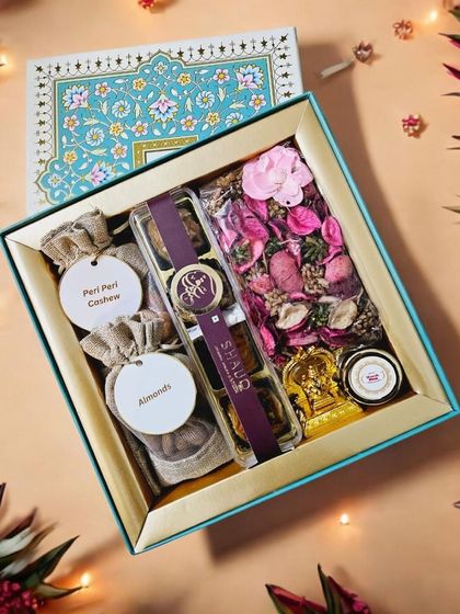 This elegant Diwali hamper features a beautiful turquoise box with intricate patterns. Inside, it holds Smoor baklava, jute potlis with almonds and peri-peri cashews, a small Ganesha idol, and fragrant potpourri.