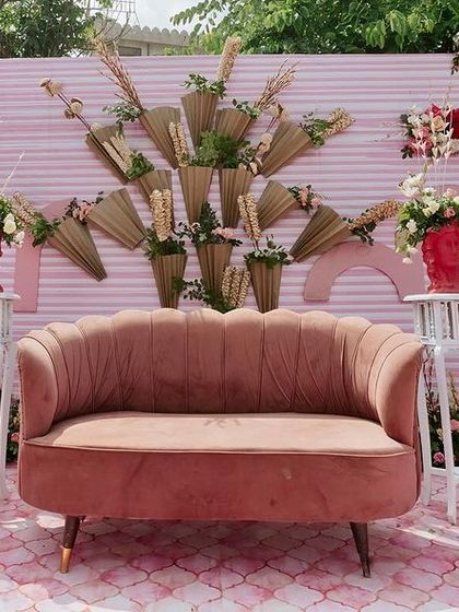 The main stage of the quirky pink Mehendi, featuring a dusty rose velvet sofa against a textured backdrop with modern art-inspired floral arrangements.