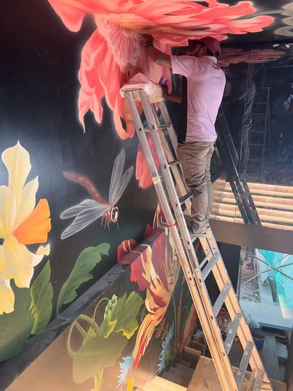 High on the ladder, the details of a dragonfly and vibrant petals come to life. This perspective shows the scale and height involved in creating such an immersive floral mural.