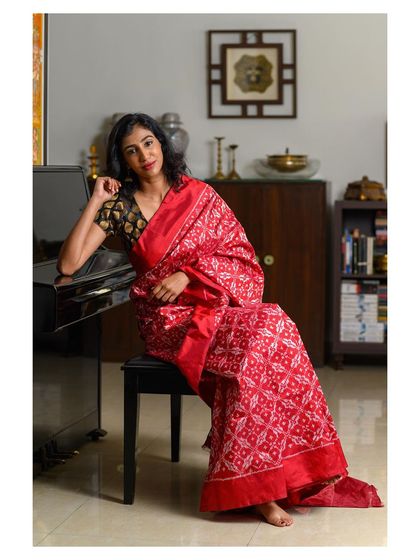 A seated portrait that allows the intricate patterns of the red saree to be the hero. This pose is perfect for lookbooks, showing how the fabric drapes while maintaining a sense of relaxed elegance.