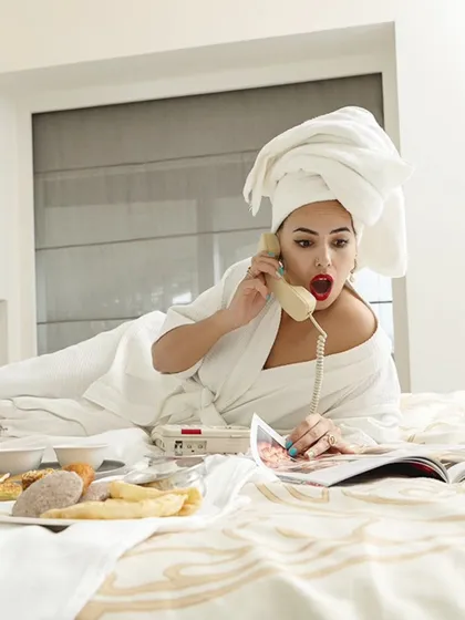 An expressive and playful shot of a model on the phone in bed. Her surprised expression adds a fun, storytelling element to the hotel lifestyle series.