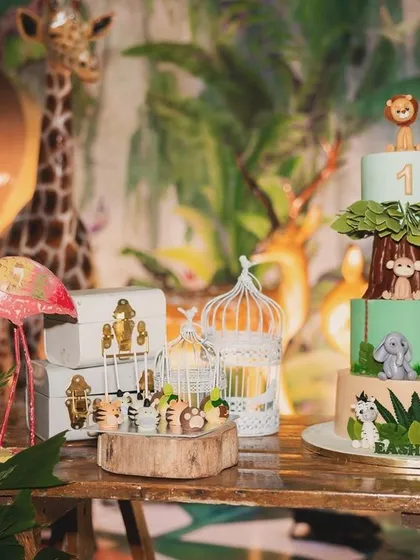The centerpiece of Eshaan's safari party: a stunning, multi-tiered jungle cake. The cake features edible animal figures and is surrounded by themed desserts and props like a miniature birdcage.