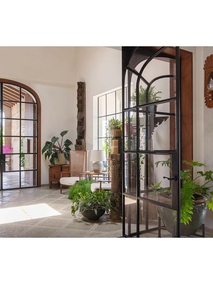 The entrance foyer is filled with potted plants and natural light, creating a welcoming, greenhouse-like feel. The design immediately establishes the home's connection to its tropical surroundings.