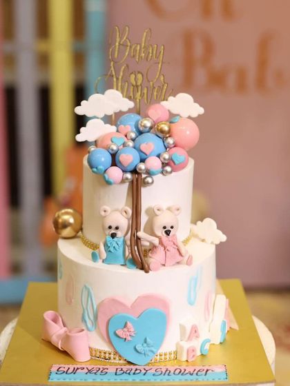 A lovely two-tiered baby shower cake with a "hot air balloon" of pink and blue spheres. The design includes cute teddy bears and baby shoes.