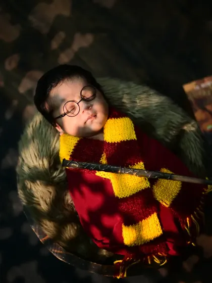A magical newborn photo with the baby dressed as Harry Potter, sleeping peacefully with a wand. The lighting creates a mystical, dreamy atmosphere.