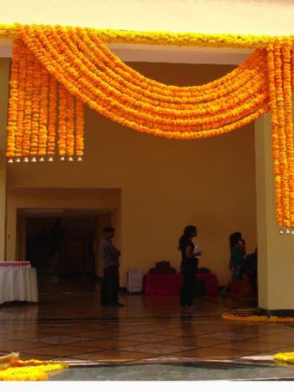 I use marigold flowers to create beautiful entrance decor for Haldi and Mehendi events. This entrance features thick garlands of orange marigolds draped across the entryway.