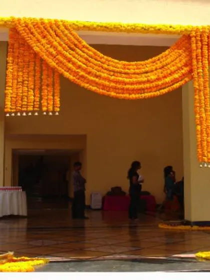 I use marigold flowers to create beautiful entrance decor for Haldi and Mehendi events. This entrance features thick garlands of orange marigolds draped across the entryway.
