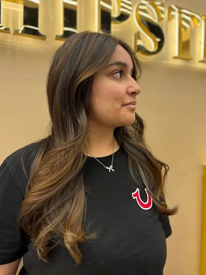 A side profile of a client with long, wavy hair and a fresh color treatment. The highlights add depth and a beautiful, natural-looking glow.