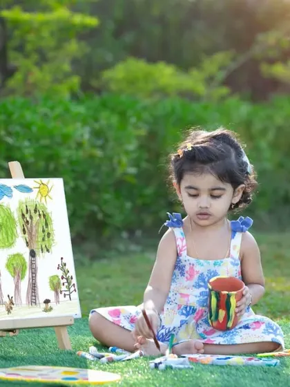 A little artist sitting in the grass, surrounded by her colorful creations.
