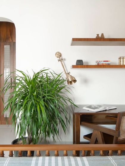 The guest bedroom includes a study corner with a teak desk and a cane-backed chair. Floating shelves provide space for books and decor, making the room multi-functional.
