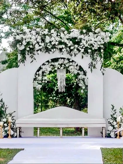 An all-white theme creates a timeless and elegant look. This outdoor stage features clean lines, modern white panels, and lush white floral arrangements, perfect for a sophisticated daytime ceremony.