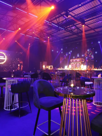 The lounge area of a high-energy party, with moody lighting and chic high-top tables, creating the perfect atmosphere for cocktails and conversation.