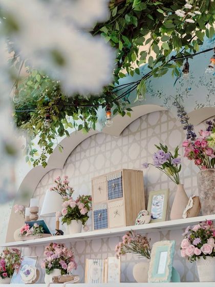 A beautifully styled shelf with floral arrangements, books, and other curated props, set against a custom-printed wallpaper.