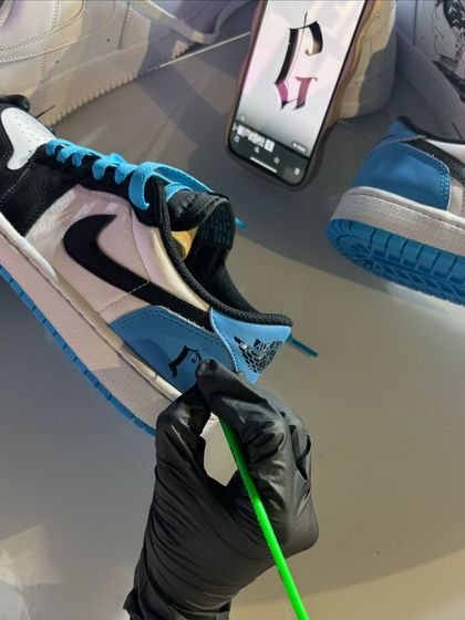 An artist carefully paints a custom initial onto a pair of Air Jordans. We use reference images on our phones to ensure every detail, like this gothic font, is perfectly executed.