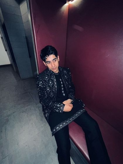 A candid shot of Ahsan Vazir seated, showcasing the detailed embroidery on the cuffs and hem of the black Indo-western kurta set.