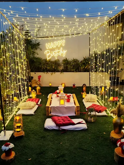 For a cozy and intimate celebration, I can create a beautiful cabana setup in your backyard. This design features a canopy of fairy lights, low picnic-style seating, and a neon sign for a personal touch.