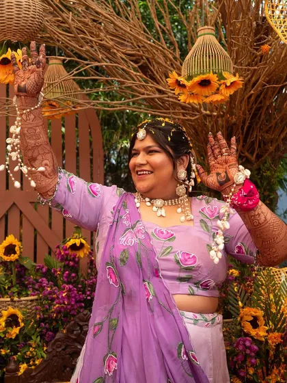 The bride, radiant in a purple lehenga, dances joyfully at her Haldi ceremony, surrounded by sunflower decor.