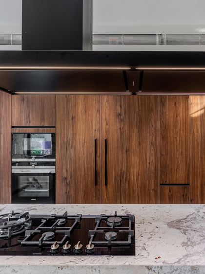 A close-up on the integrated Siemens appliances and the rich texture of the walnut wood veneer. The handleless design maintains the kitchen's sleek and modern profile.
