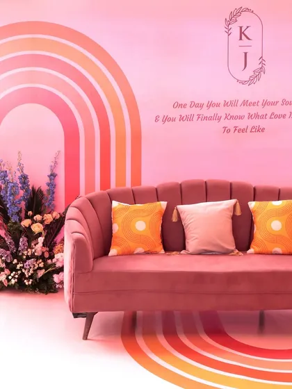 A chic seating nook with a pink velvet sofa, set against a wall with rainbow graphics and the couple's monogram, creating a personalized and trendy photo spot.