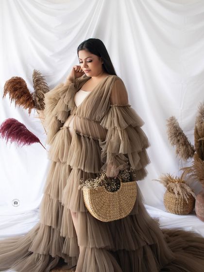 A stylish boho-glam look, featuring a layered beige gown and a woven handbag, set against a backdrop of pampas grass.