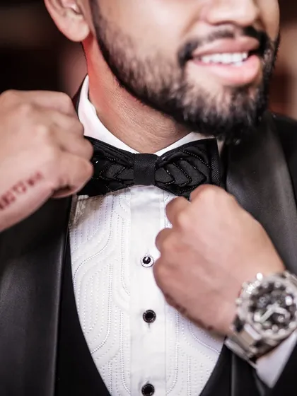 A close-up shot focusing on the details of the groom's attire: the texture of his bow tie, his watch, and the hint of a tattoo on his hand.