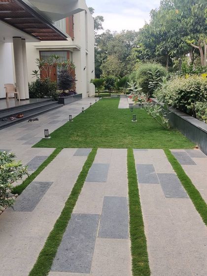 A modern walkway design for an urban residence, using large stone pavers interspersed with strips of green lawn. This hardscaping technique breaks up the solid surface, allowing for better water drainage and integrating greenery into the pathway itself.