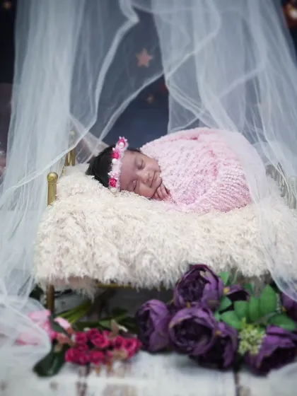 A princess asleep in her royal bed. This newborn is wrapped in pink, sleeping on a miniature four-poster bed with a delicate canopy.
