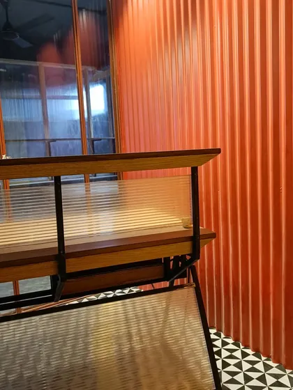 A detail shot from the New Delhi office, highlighting the material contrast between the corrugated orange wall, fluted glass partition, and the custom wooden desk with a steel frame.