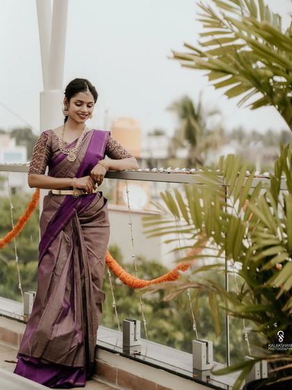 A bride posing on a rooftop, her purple saree standing out against the sky.