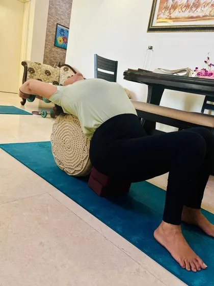This is a modification for the shoulder stretch, using a bolster and yoga blocks for support. This setup allows the body to relax into the pose, which is key for releasing tension in the upper back and shoulders.