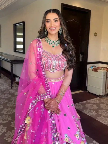 A full view of the vibrant pink Mehendi look. The mirror-work lehenga is perfectly complemented by the soft and glowing makeup.