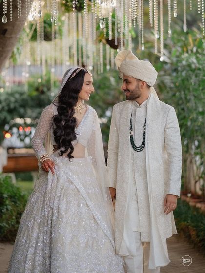 A beautiful portrait of a couple in matching white wedding attire. Their joyful interaction and the elegant decor create a light and airy feel, perfect for a daytime wedding ceremony.