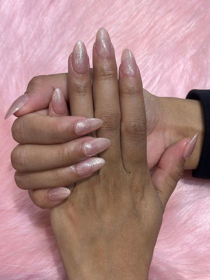 A simple yet stunning set of long, almond-shaped nails with a subtle, shimmery pink glitter polish.