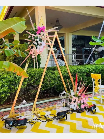 A modern decorative element for a Haldi ceremony. This triangular wooden frame is adorned with pastel flowers and bird cages, creating a chic photo corner.