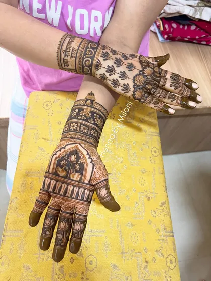 A unique bridal design where one hand is fully intricate with palace architecture, while the other features a simpler pattern with a meaningful Sanskrit quote.