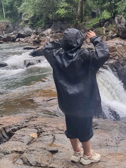 A traveler in a raincoat stands by a rushing stream in Wayanad, fully immersed in the monsoon experience.