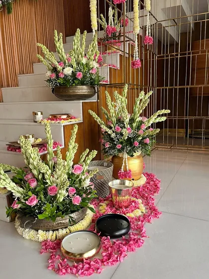 A beautiful staircase decorated for a festive Diwali event. The steps are adorned with brass urns filled with tuberoses and pink roses, scattered petals, and elegant candles, creating a luxurious and welcoming sight.