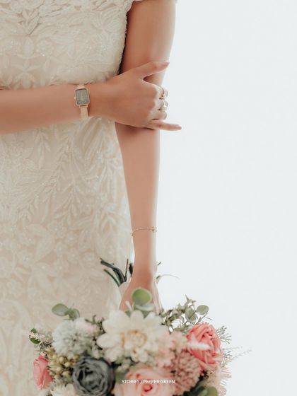 A close-up detail shot of the bride's hands, watch, and bouquet, capturing the small, elegant details of her wedding day look.