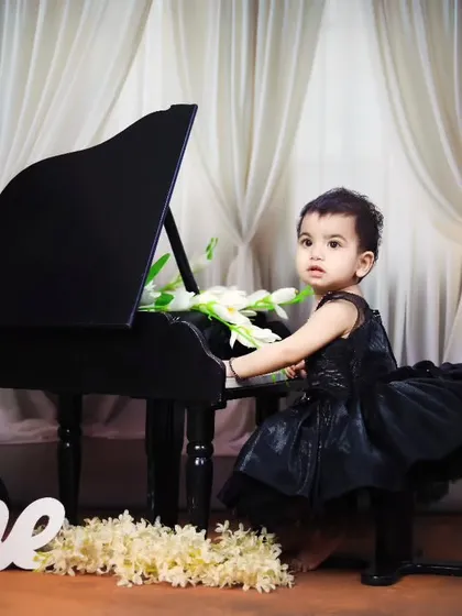 An elegant first birthday shoot with a baby girl in a black dress at the piano.