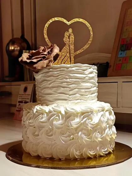 A romantic two-tier anniversary cake with textured buttercream and rosette piping, topped with a single sugar rose and a couple silhouette.